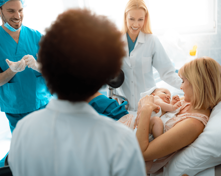 Mother holding newborn in hospital with doctors.