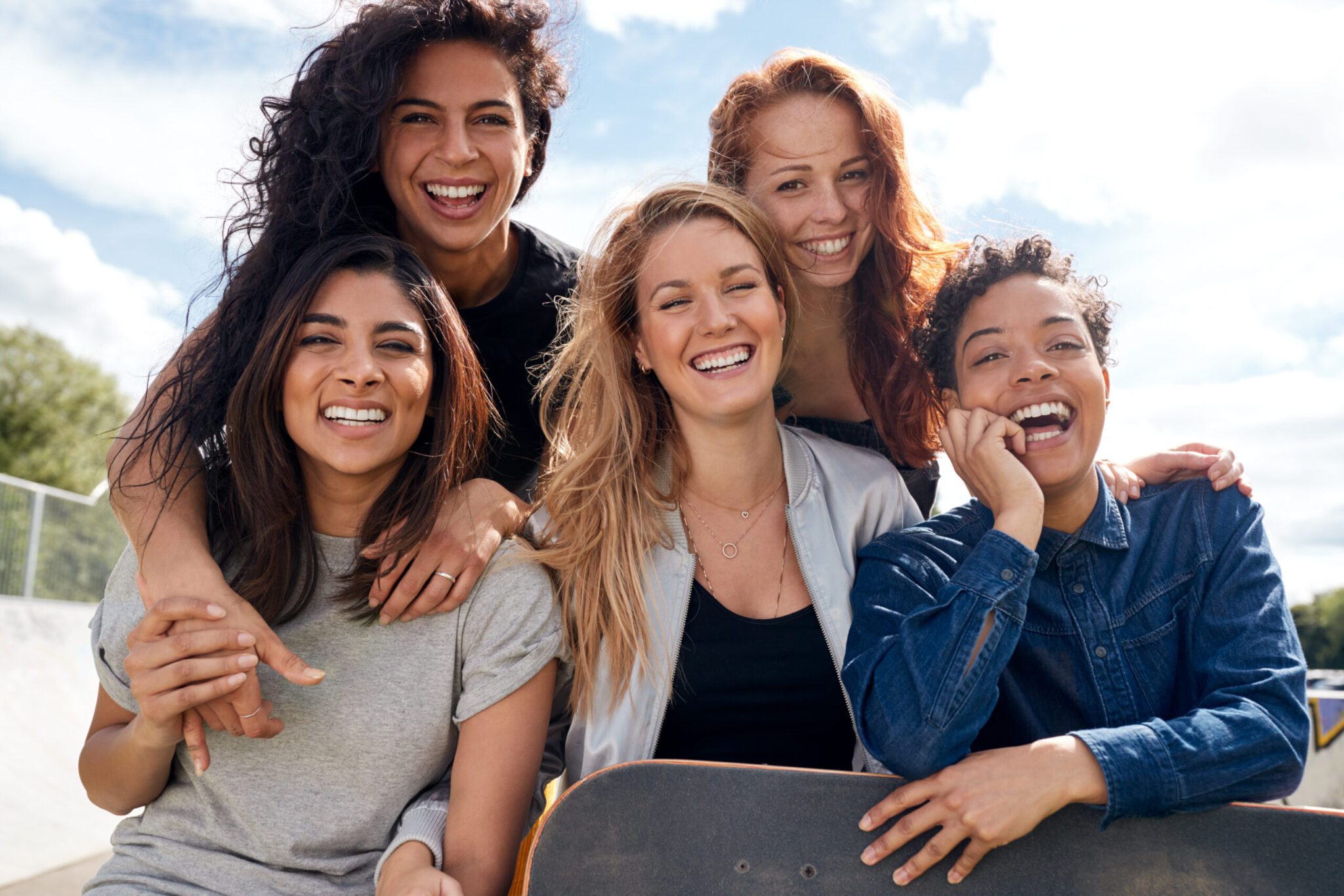 Five friends smiling outdoors with skateboard